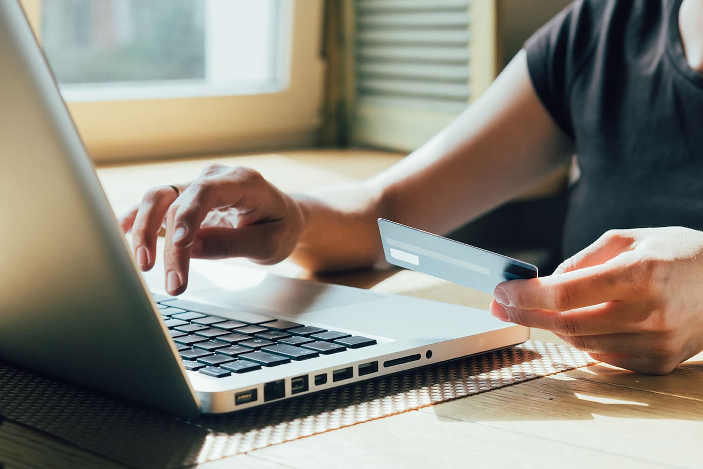 A photo of someone using their laptop while holding a credit card in one hand